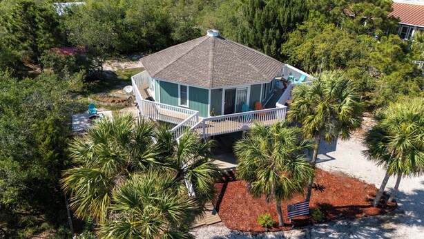 A two-story house with a wrap-around porch, surrounded by palm trees and a sandy area. - Beach Joy! GOLF CART included! 2-min BEACH walk, Sleeps 6!! (St. George Island)