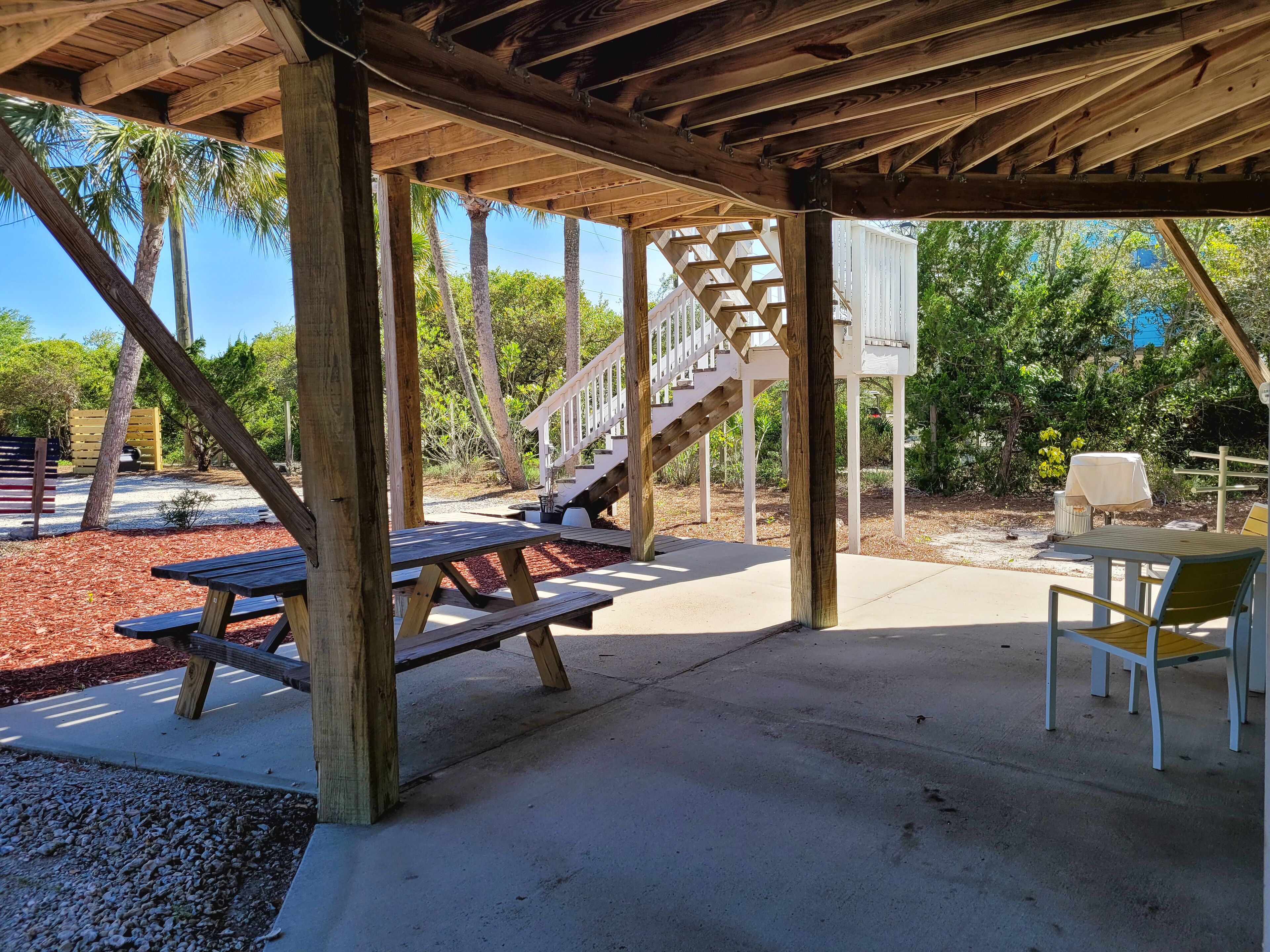 Un patio techado al aire libre con mesas de picnic y una escalera que lleva a un edificio blanco.