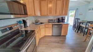 A modern kitchen with wooden cabinets, stainless steel appliances, and a bar area with stools. - Beach Joy! GOLF CART included! 2-min BEACH walk, Sleeps 6!! (St. George Island)