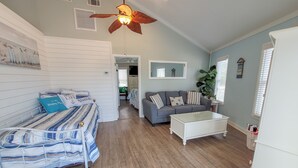 A spacious living room with a sofa, a coffee table, and a bed with striped bedding. - Beach Joy! GOLF CART included! 2-min BEACH walk, Sleeps 6!! (St. George Island)