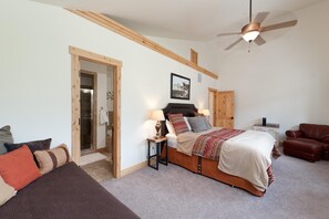 Ein Schlafzimmer mit einem Bett, einem Deckenventilator, einer Holztür, einem kleinen Tisch mit Lampe und einem braunen Ledersessel.