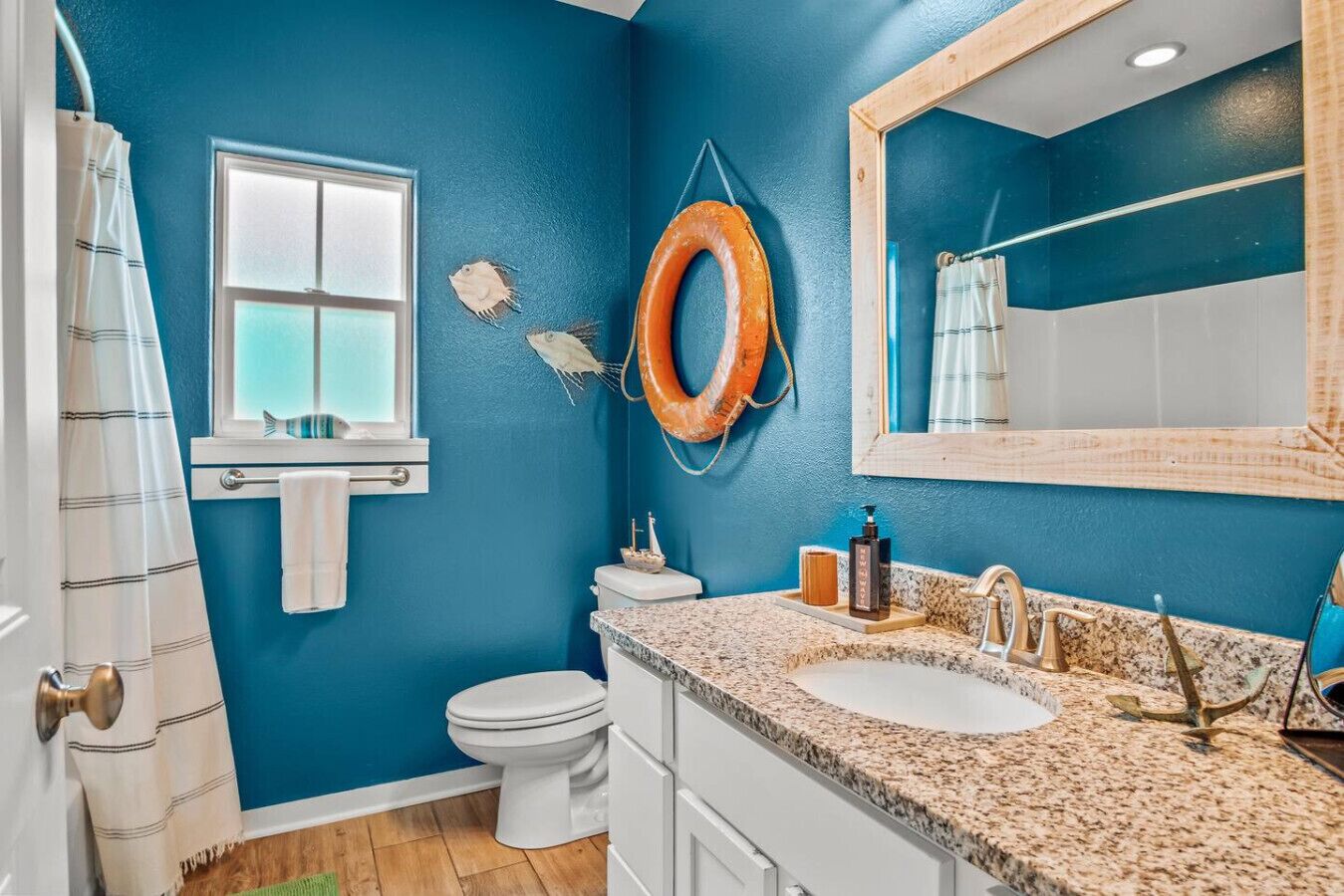 A bathroom with a blue wall, a white toilet, a sink with a granite countertop, and a mirror above the sink.