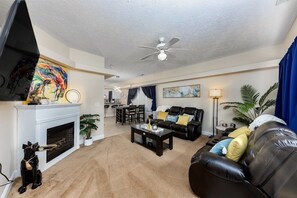 A living room with a fireplace, a ceiling fan, a dining area, and a kitchen in the background. - 5 minutes to Cherry point! Family-sized townhouse with fireplace & balcony (Havelock)