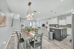 A modern kitchen with a central island, a dining area with a table and chairs, and a staircase leading to another level. - 🍊 Home Away from Home (Houston)