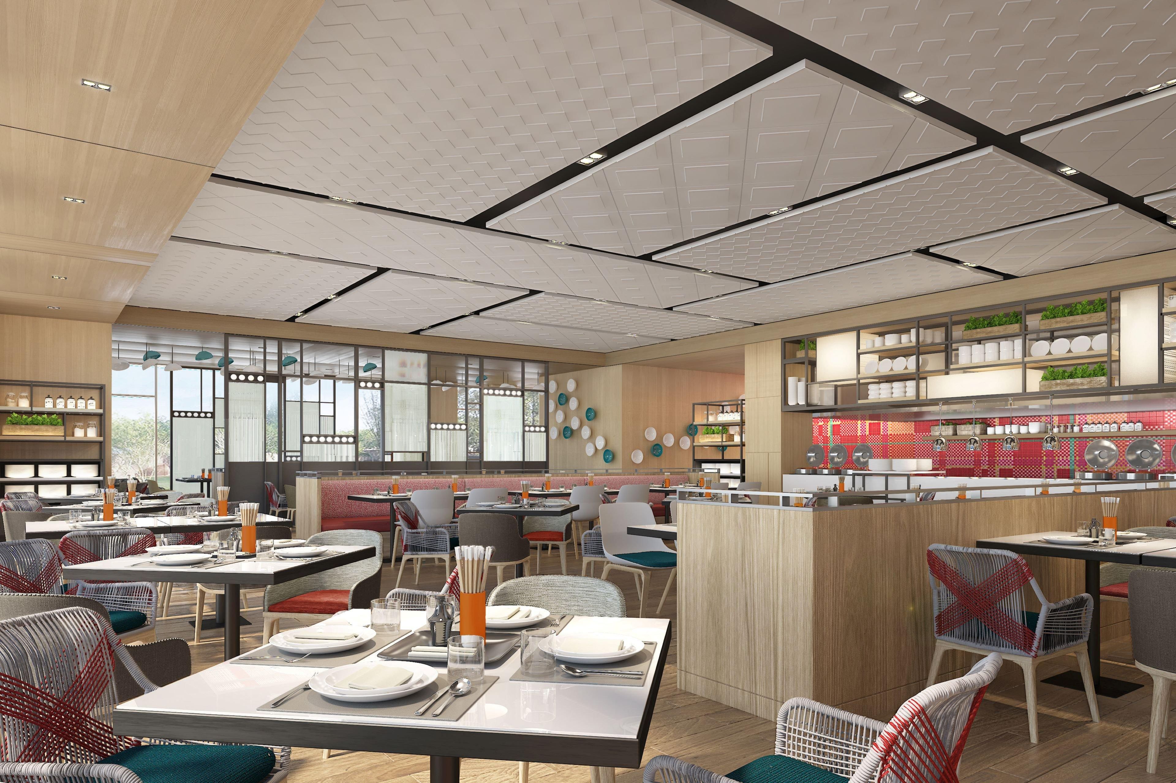 Un intérieur de restaurant moderne, caractérisé par de hauts plafonds, de grandes fenêtres et une variété d’agencements de sièges.
