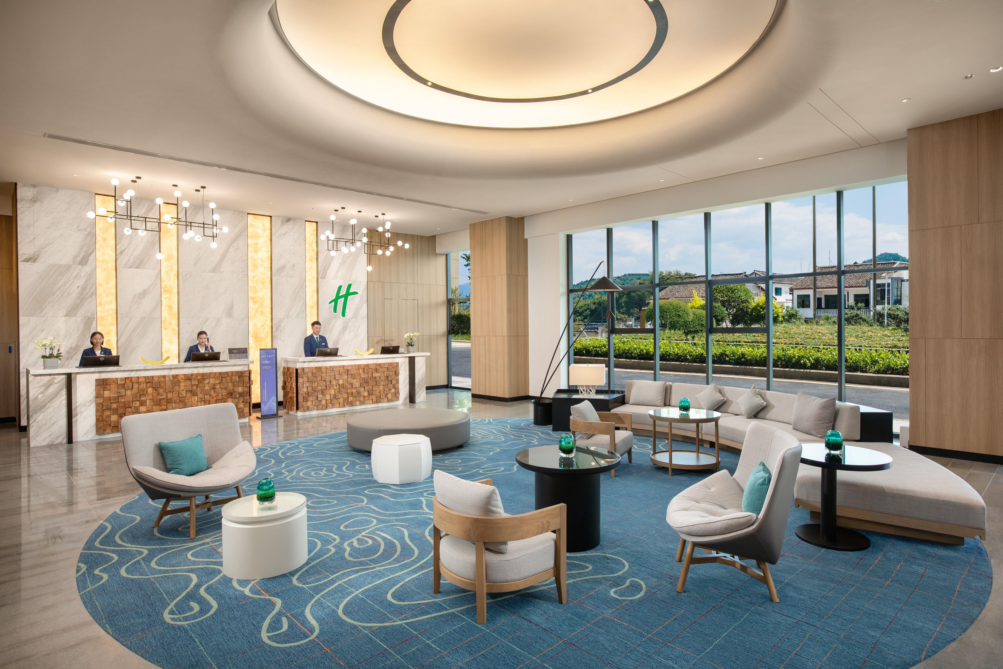 A modern hotel lobby with a reception desk, seating area, and large windows offering a view of the outdoors.