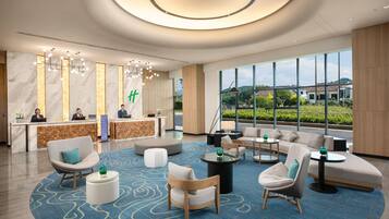 A modern hotel lobby with a reception desk, seating area, and large windows offering a view of the outdoors.