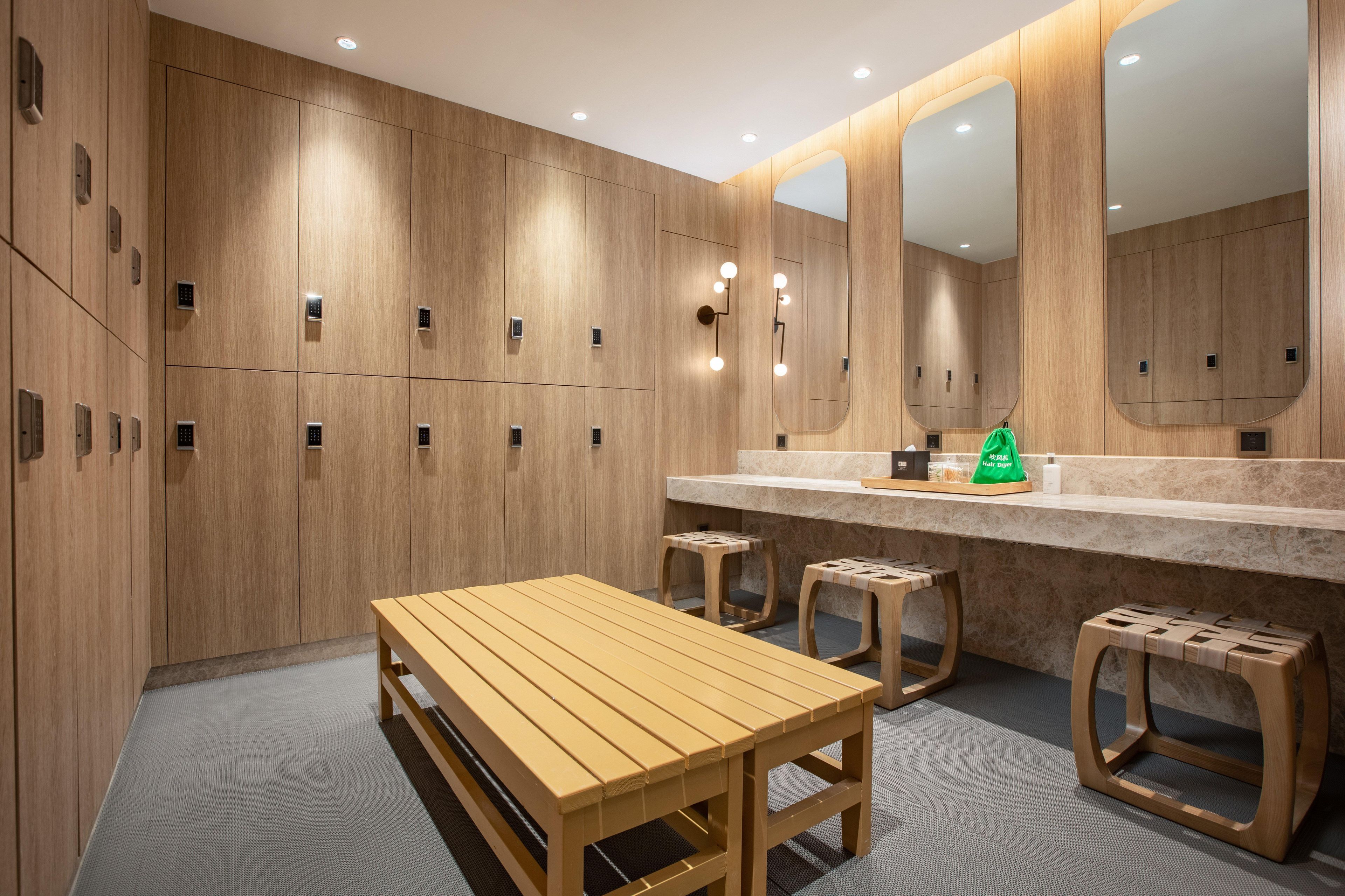 Un vestuario con taquillas de madera, un banco y una zona de tocador con espejo e iluminación.
