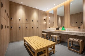 Un vestiaire avec des casiers en bois, un banc et un coin coiffeuse équipé d’un miroir et d’un éclairage.
