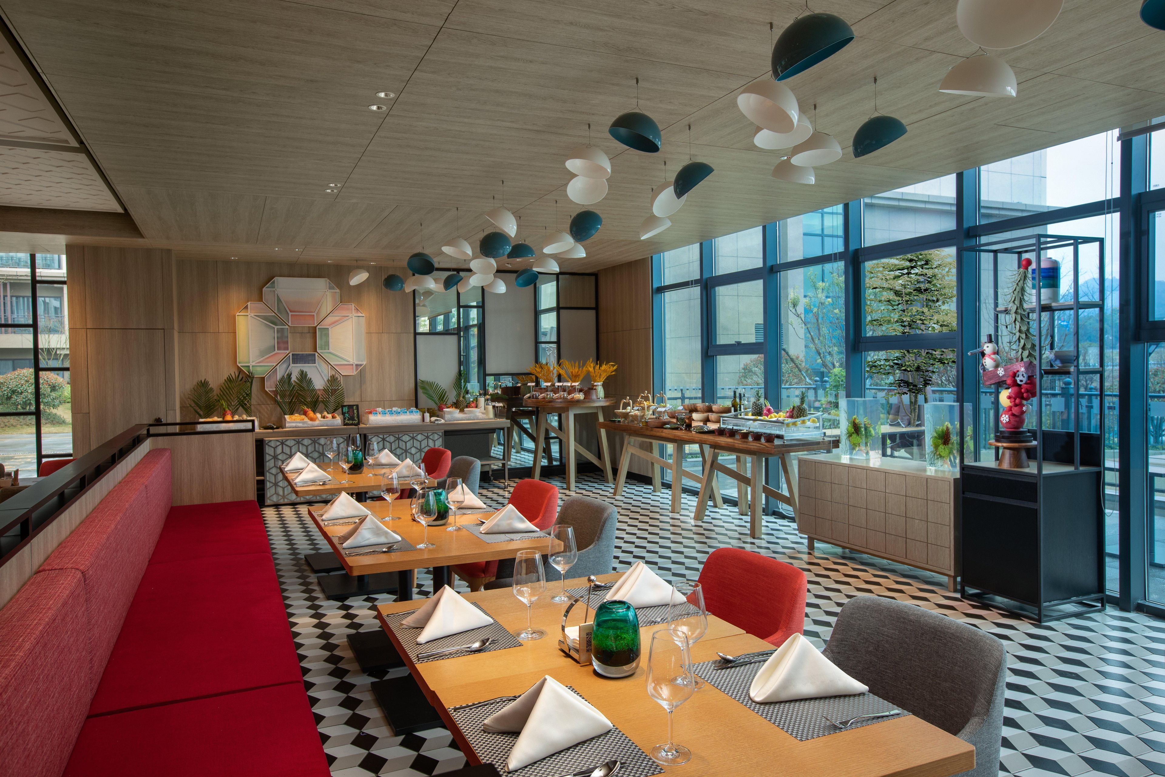 A modern restaurant with wooden tables, red seating, and large windows.