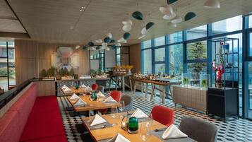 A modern restaurant with wooden tables, red seating, and large windows.