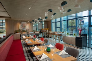 A modern restaurant with wooden tables, red seating, and large windows.