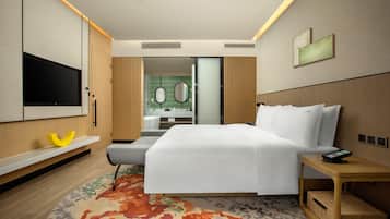 A hotel room with a bed, a TV, a bedside table, a mirror, and a bathroom visible through an open door.