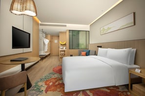 A modern hotel room with a bed, a TV, a desk, and a chair.