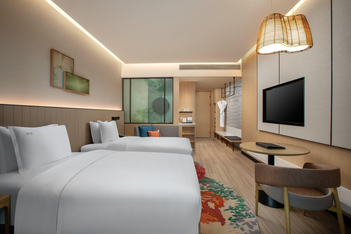 Una habitación de hotel moderna con dos camas, un televisor, una mesita pequeña y una silla.