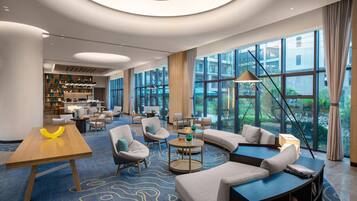 A modern hotel lobby with a curved sofa, round tables, and a large window offering a view of the outdoors.