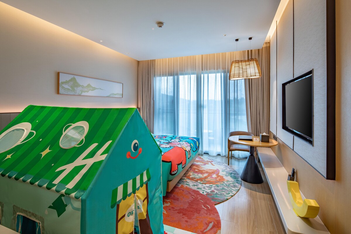 Una habitación de hotel con cama, televisor, casita de juegos, silla y mesa.