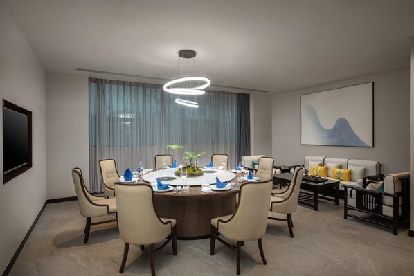Un comedor moderno con una mesa redonda, sillas, una araña y un sofá, junto con un cuadro abstracto de gran tamaño en la pared.