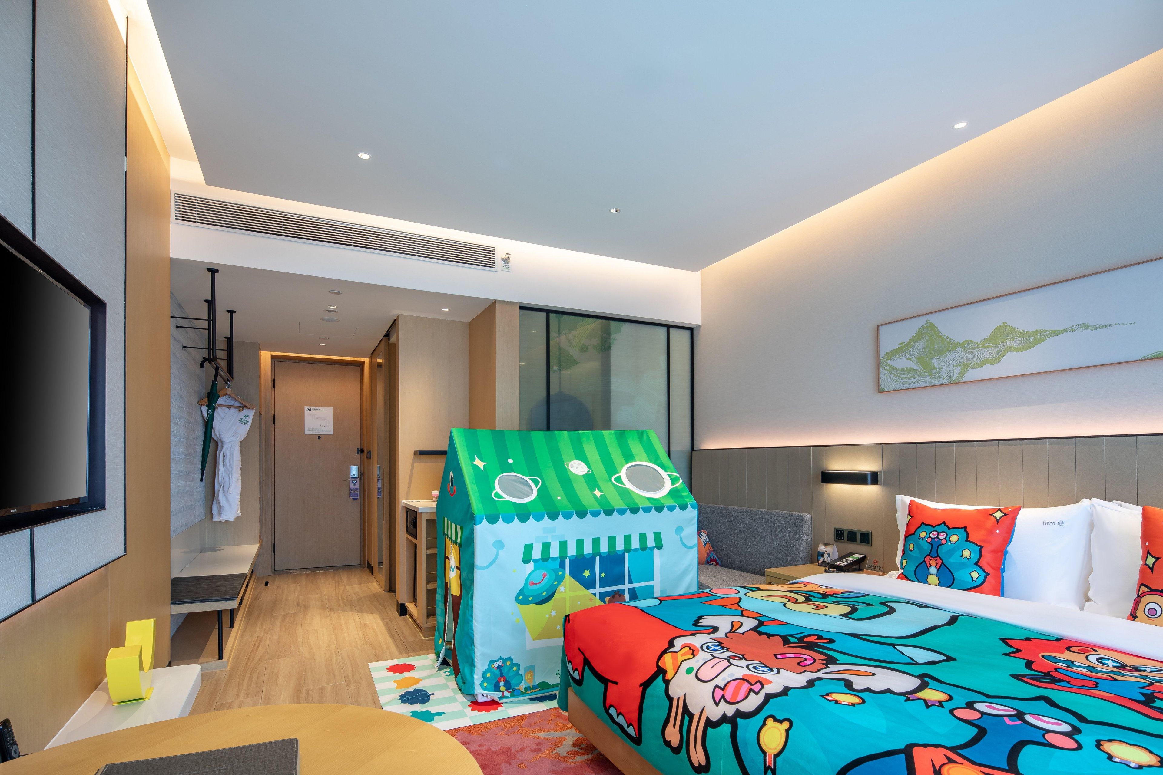A modern hotel room with a bed, a playhouse, a TV, and a large window.