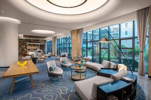 A modern hotel lobby with a curved sofa, round tables, and a large window offering a view of the outdoors. - Holiday Inn Resort Guiyang Qingyan (Guiyang)
