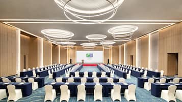 Un salón de conferencias con filas de mesas, sillas y una gran pantalla al frente.