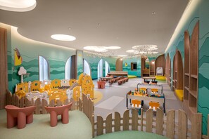 Una sala de juegos infantiles con un corralito de madera, mesas, sillas y un mural en las paredes.