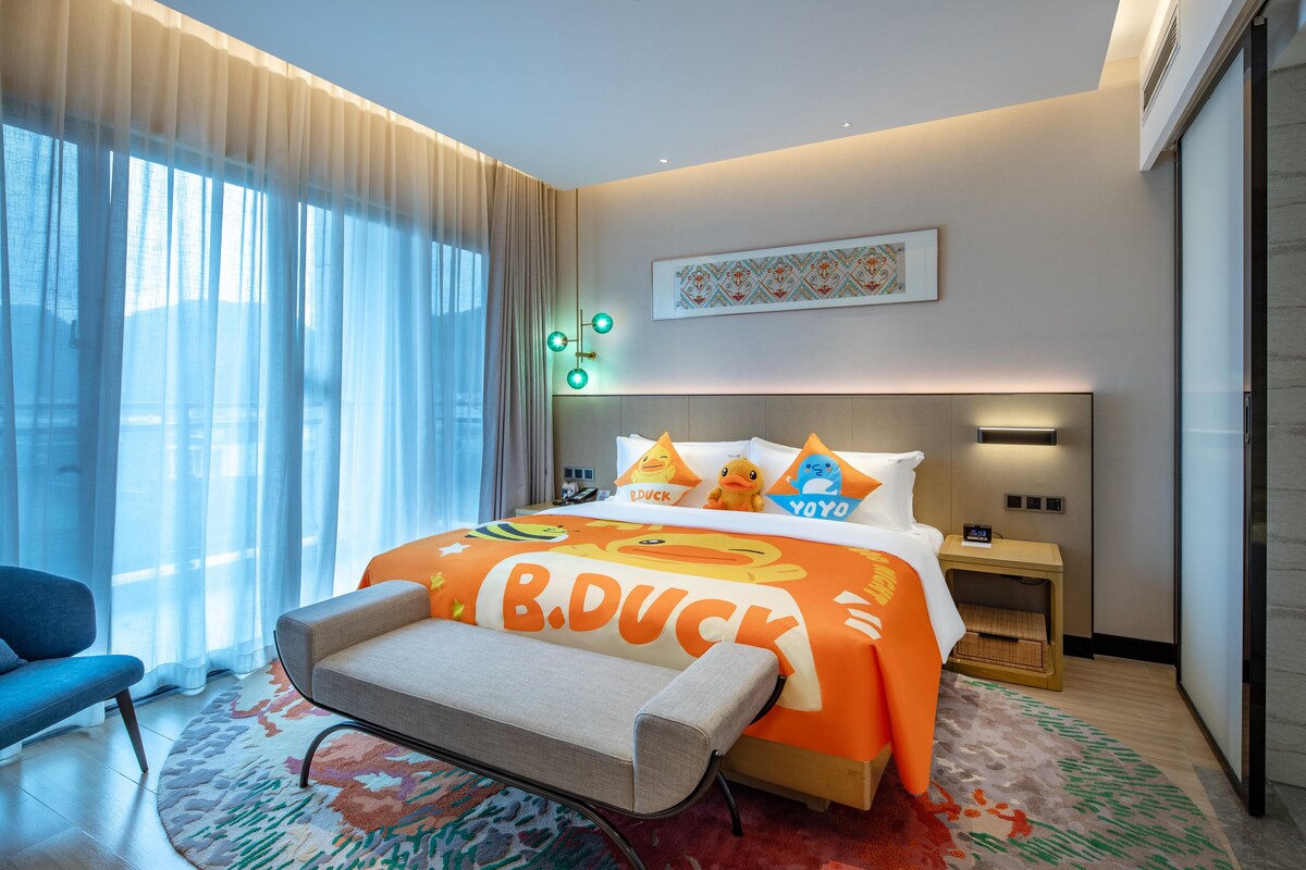 Habitación de hotel con cama, escritorio, silla, ventana con cortinas y una obra de arte en la pared.