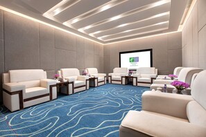A conference room with a large screen, multiple sofas, and a patterned carpet.