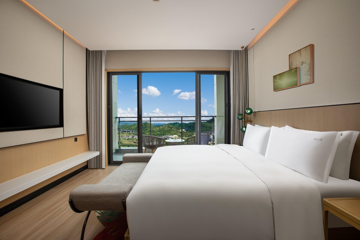 Habitación de hotel con una cama grande, un televisor de pantalla plana, un balcón con vistas y un cuadro en la pared.