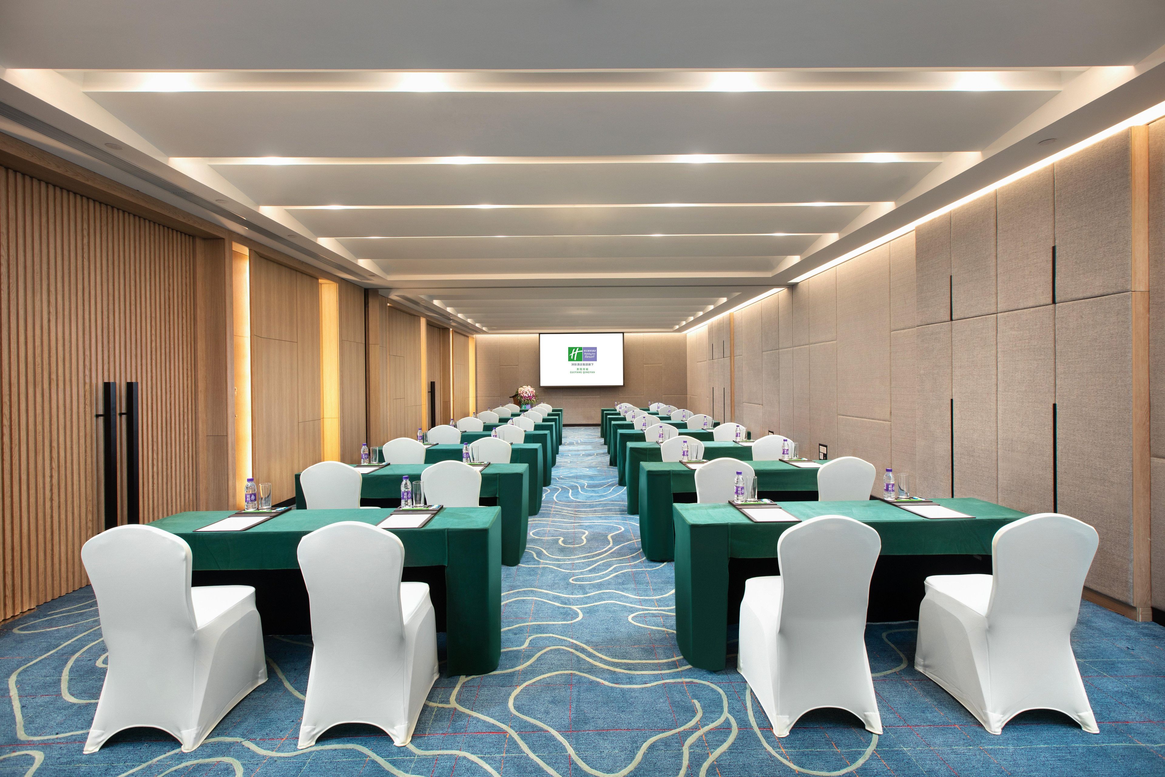 A conference room with rows of tables, chairs, and a screen at the front.