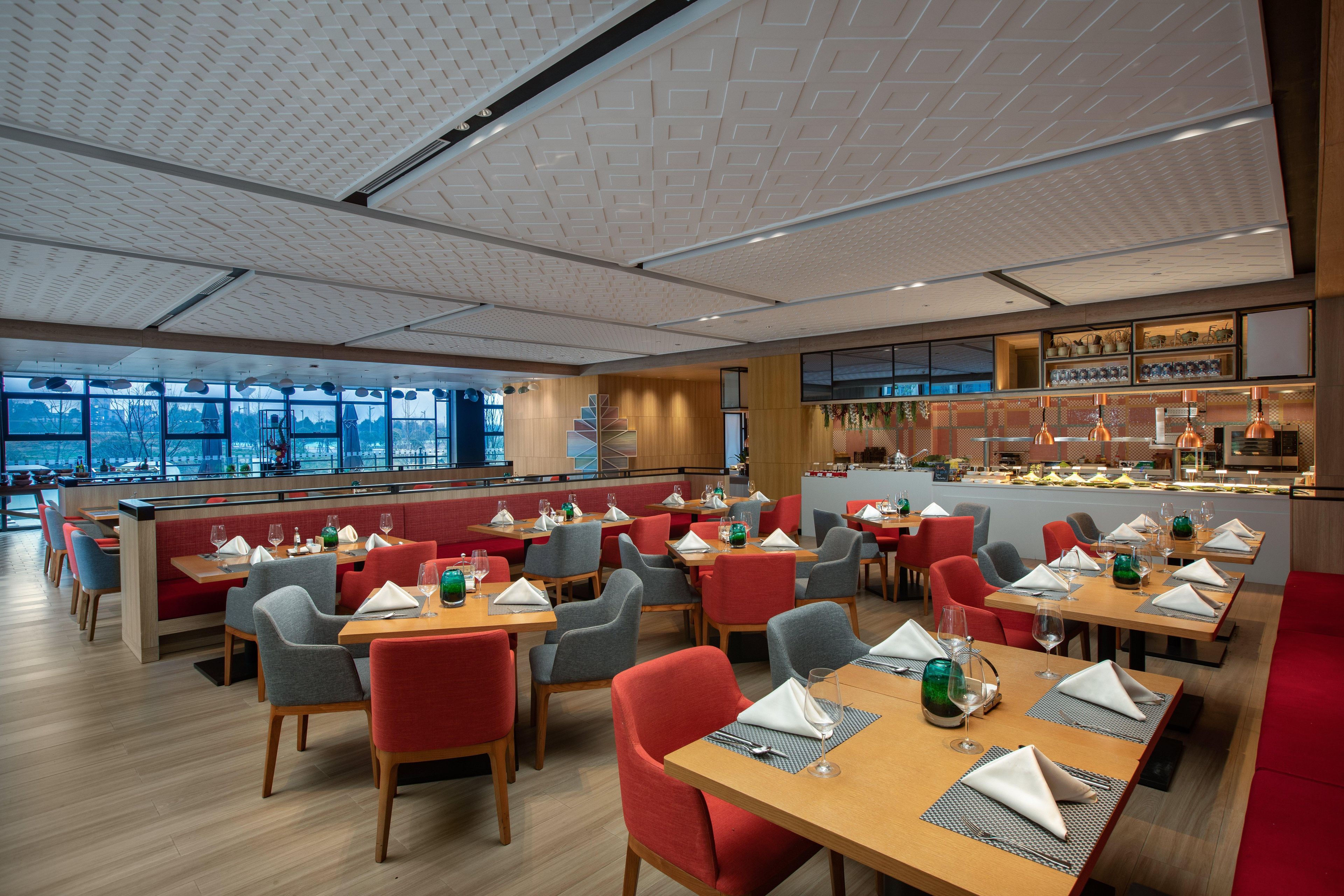 Un restaurant moderne doté de nombreuses tables et chaises, d’un bar et de grandes fenêtres offrant une vue panoramique.