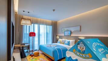 Una habitación de hotel con cama, escritorio, silla, aro de baloncesto y un tapete de juego colorido.