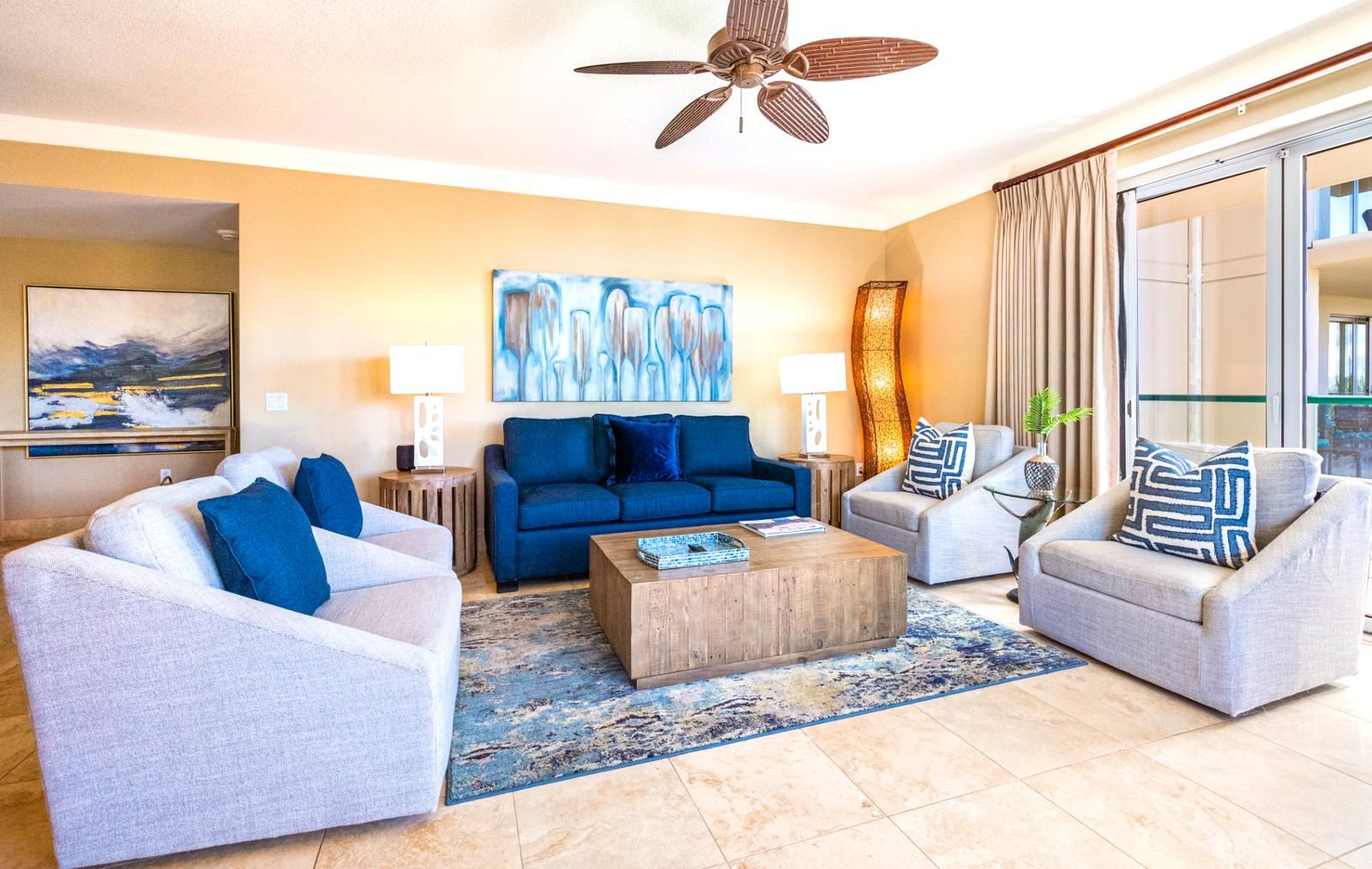 Ein modernes Wohnzimmer mit einem blauen Sofa, zwei Sesseln, einem Couchtisch und einem Deckenventilator.