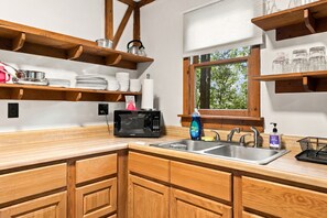 A kitchen with wooden cabinets, a built-in microwave, a sink with a faucet, and shelves above the counter holding dishes and a kettle.