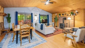 A cozy cabin interior with a dining area, sofa, fireplace, and a ceiling fan.