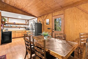 Un interior de madera con una mesa de comedor, sillas, un refrigerador y una zona de cocina con armarios de madera y una ventana.