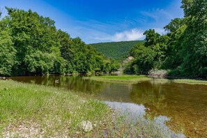 A river surrounded by dense greenery and a hill in the background. - River Cabin w/ Hot Tub, Screened Porch & Fire Pit (Great Cacapon)