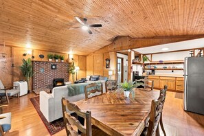 A spacious living area with a fireplace, a dining table, and a kitchen area with wooden cabinets and a refrigerator.