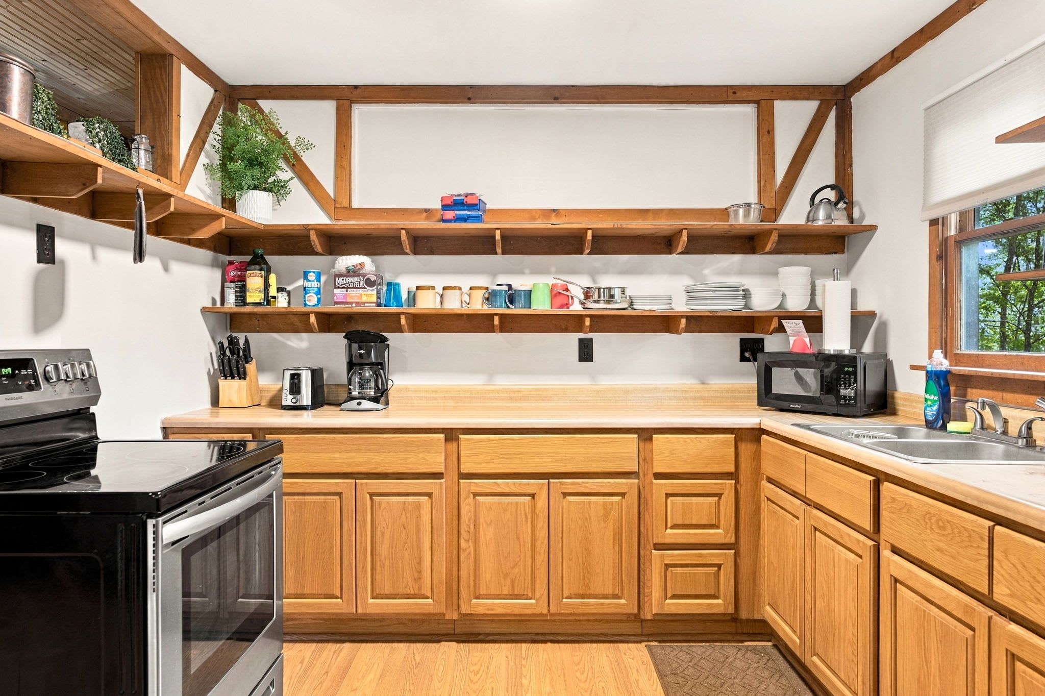 A kitchen with wooden cabinets, a stove, a microwave, and various kitchen items on shelves.
