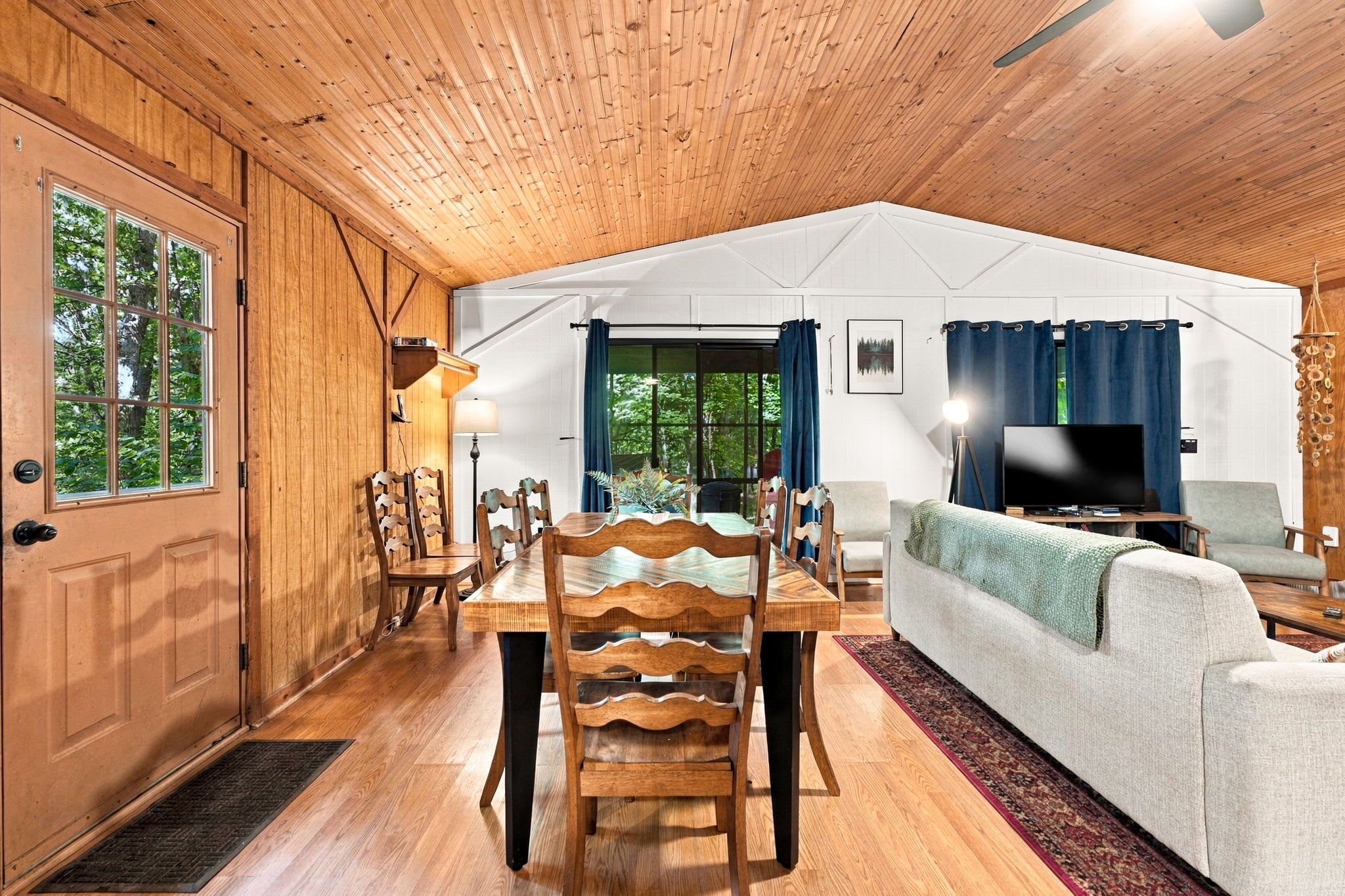 A wooden interior with a dining area, sofa, and TV.