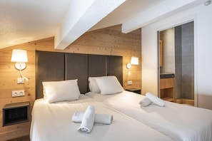 Quarto de hotel com cabeceira de madeira, duas camas, abajures, prateleira embutida e uma janela grande.