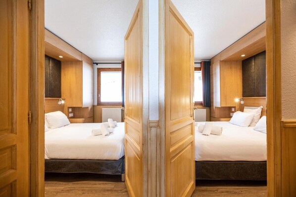 A hotel room with two beds, wooden paneling, and a window providing natural light.