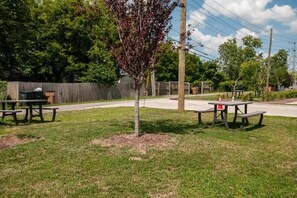 A picnic area with two tables and benches, surrounded by grass and trees.