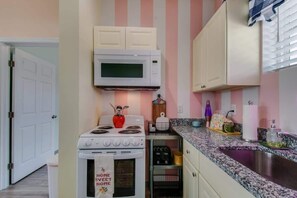 A kitchen with a white stove, a microwave, and a sink. There is a door leading to another room. - East Nashville pop-art apartment, sleeps 12, 4BR near downtown (Nashville)