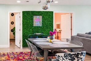 Un comedor con una pared verde, un cartel enmarcado y una mesa con manteles individuales y sillas.