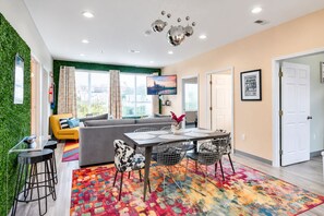 Una sala moderna con sofá, mesa de comedor y sillas, una pared verde y vistas a la ciudad.