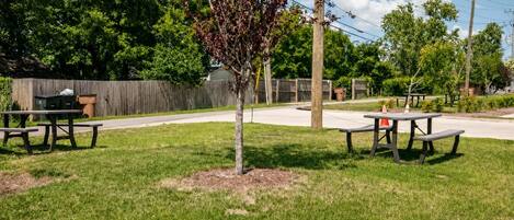 Un espace pique-nique avec deux tables et des bancs, entouré de pelouse et d’arbres.
