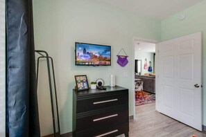 A room with a flat-screen TV mounted on the wall, a black dresser with drawers, a framed photo, and a hanging macrame wall hanging.