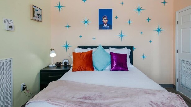A bedroom with a bed, a nightstand, a lamp, and a wall with star decorations.