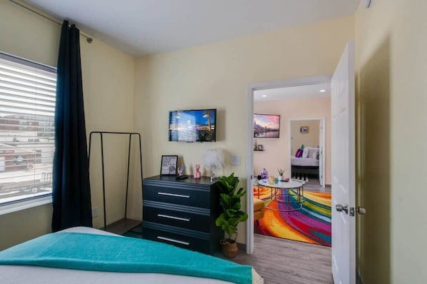 Un cuarto de hotel con una cama, un escritorio con cajones, un televisor en la pared, una ventana con cortinas y vistas a la ciudad.